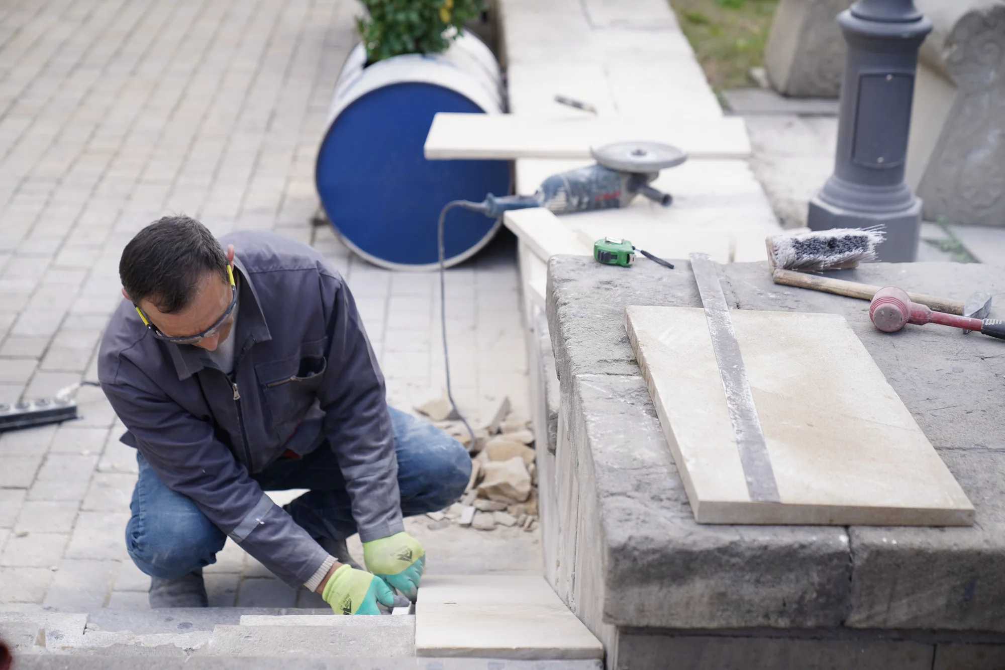 Handwerker in grauer Jacke setzt draußen eine helle Steinplatte an einer Mauer